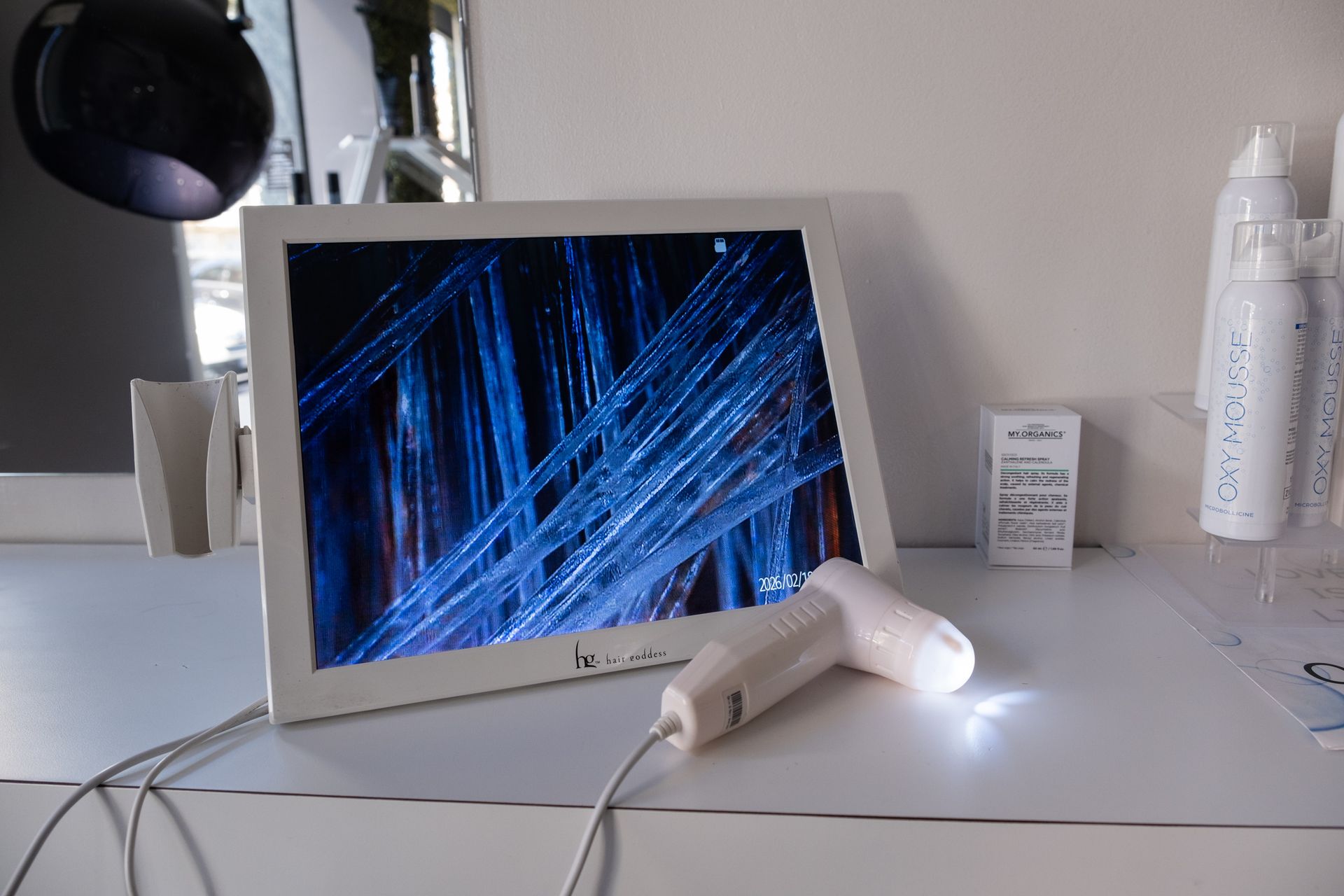 Un display digitale bianco di un microscopio che mostra fibre di capelli blu ingrandite, con la sonda della fotocamera portatile appoggiata davanti.