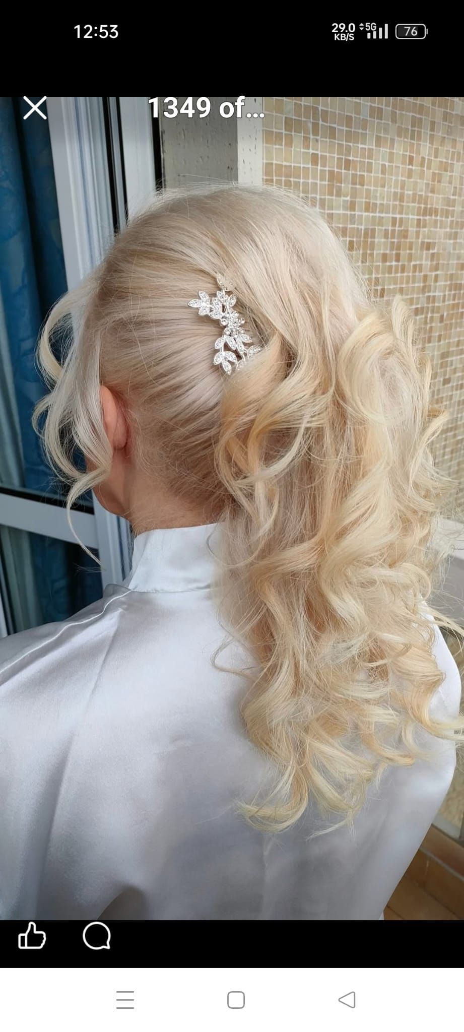 Una persona con lunghi capelli biondi e ricci, raccolti in una mezza coda e fermati da una molletta decorativa argentata.