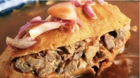 Un primer plano de un sándwich con carne y cebolla en un plato.