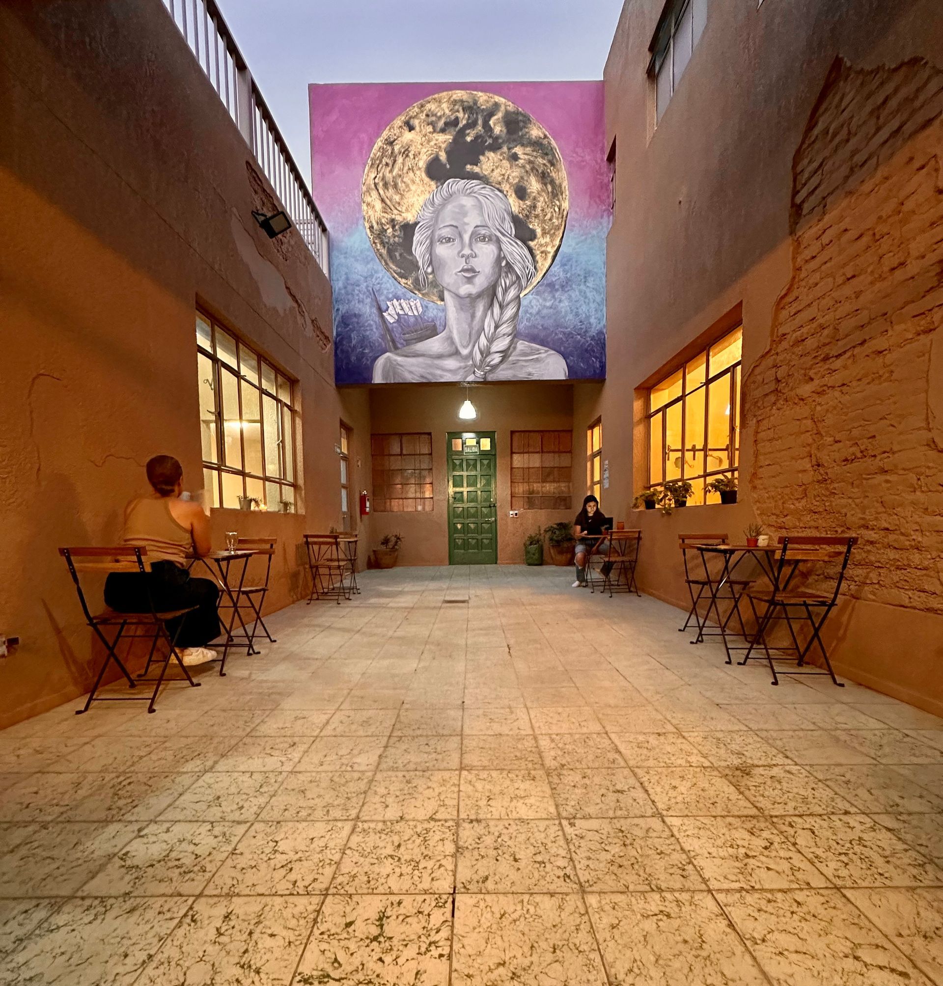 Una mujer se sienta en una mesa frente a un gran mural de una mujer.