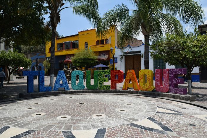 Un letrero colorido que dice Tlaquepaque frente a un edificio amarillo.