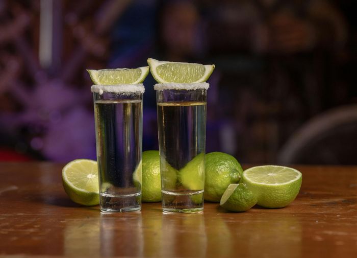 Dos tragos de tequila con rodajas de lima sobre una mesa de madera.