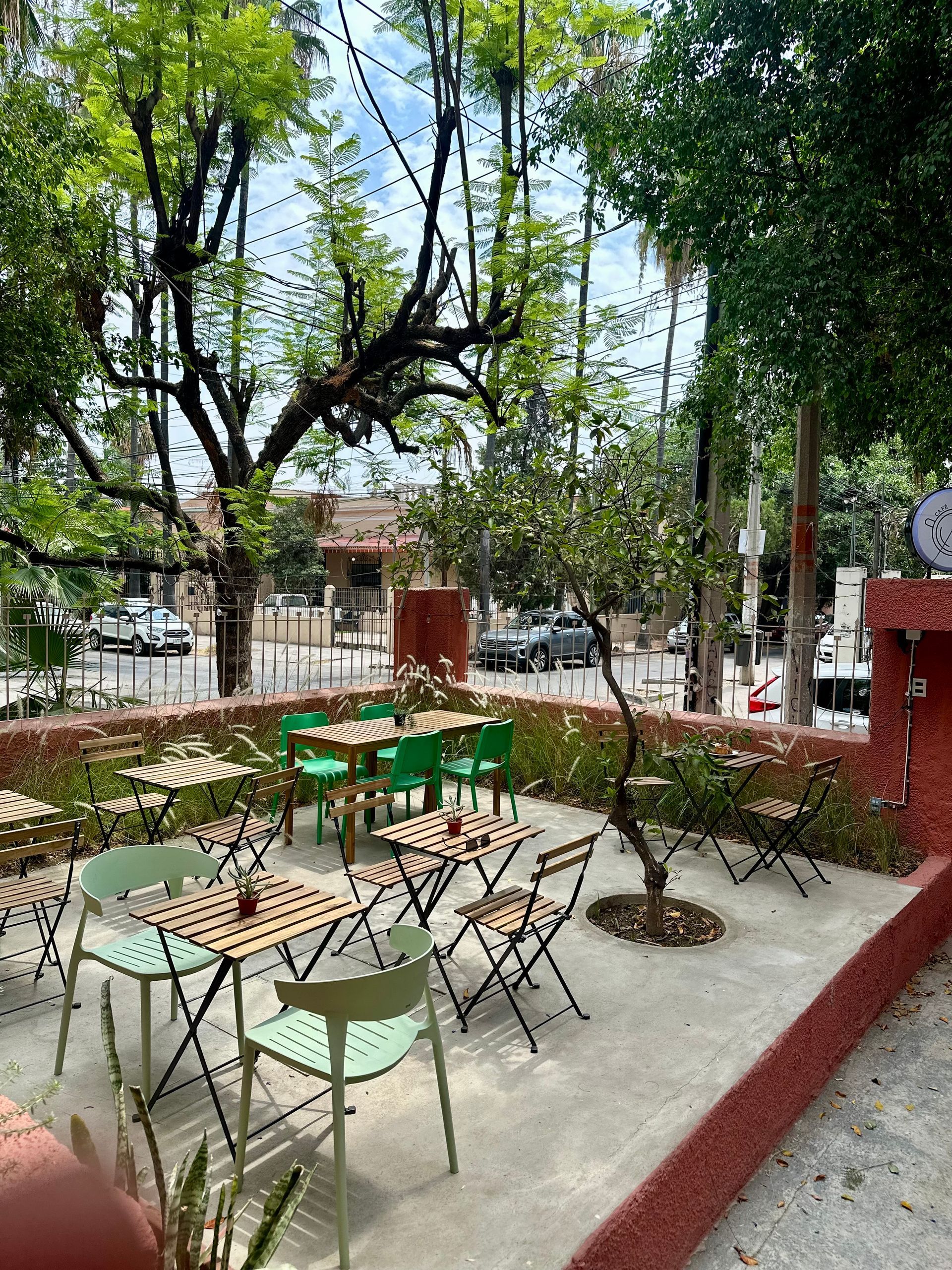 Un patio con mesas y sillas rodeado de arboles.