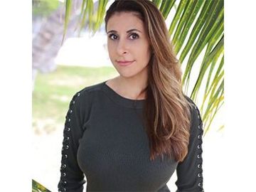 Woman in a black top standing outdoors with green palm leaves in the background