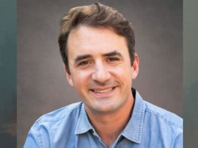 Smiling man in a light blue shirt against a gray studio background