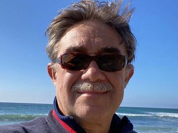 Man wearing sunglasses smiling at the beach with ocean and blue sky behind him