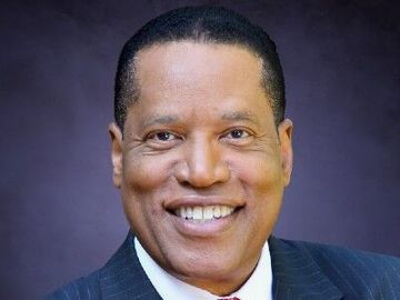 Smiling man in a dark suit and purple tie against a purple background