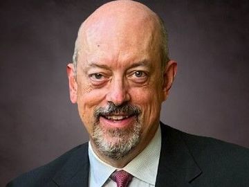 Smiling bald man in a dark suit and red tie against a gray background