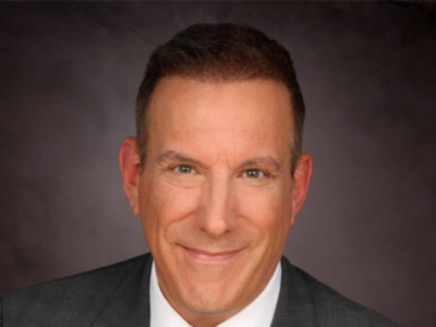 Studio portrait of a smiling man in a dark suit against a gray background