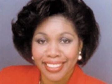 Smiling portrait of a woman with dark hair wearing a bright red top against a gray background