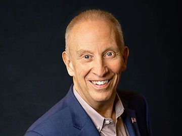 Portrait of a smiling person in a blue blazer against a dark background