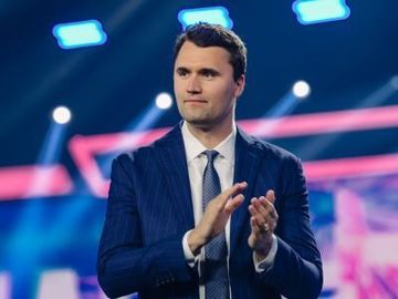 Man in a blue suit applauding on a brightly lit stage with pink and blue lights