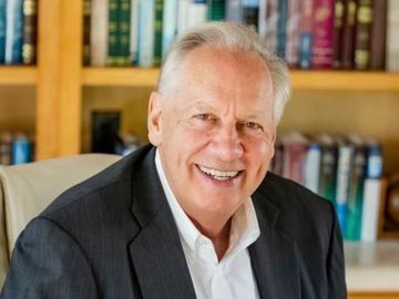 Smiling man in a dark suit seated in front of a bookshelf backdrop