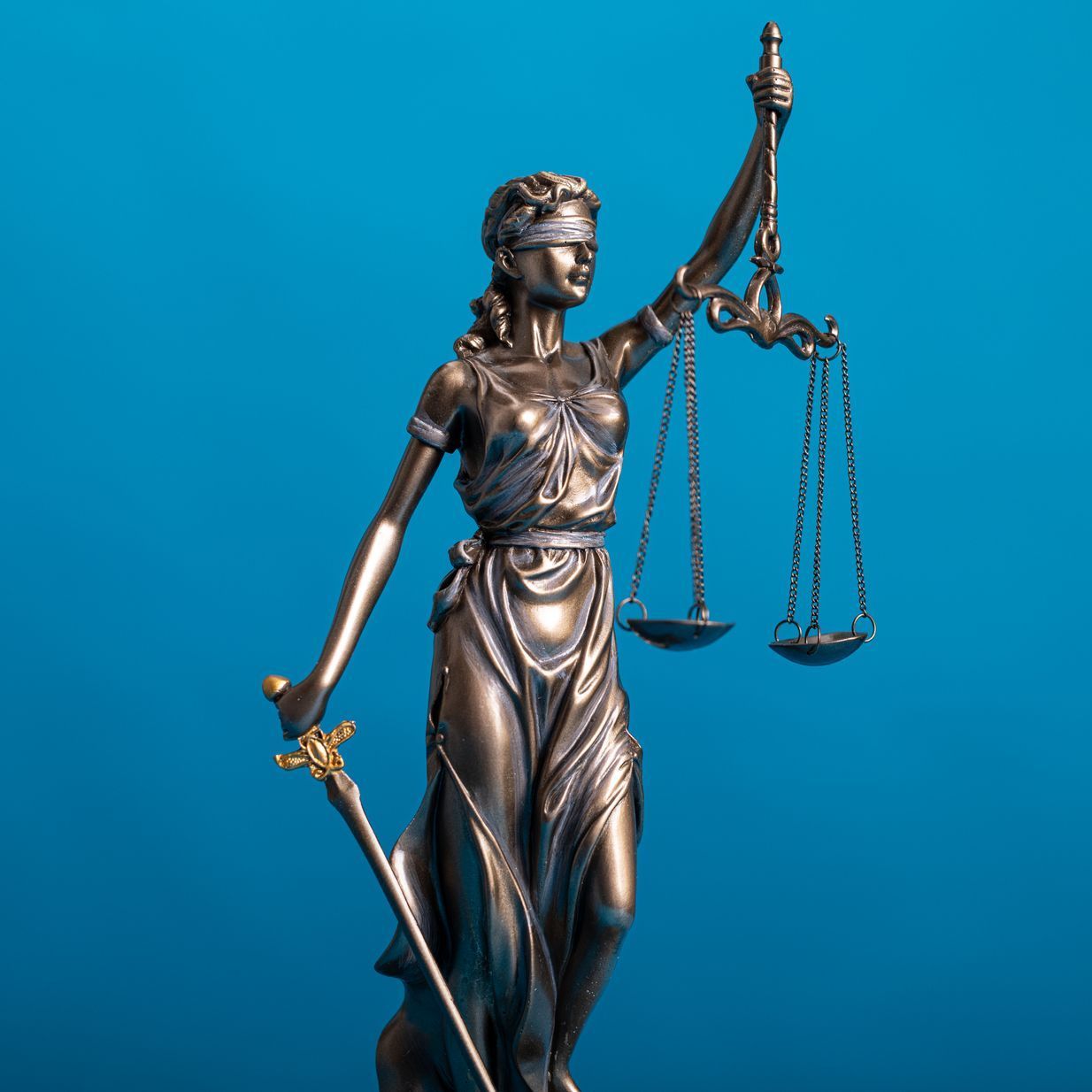 Statue of Lady Justice with scales and sword, blindfolded, on a blue background.