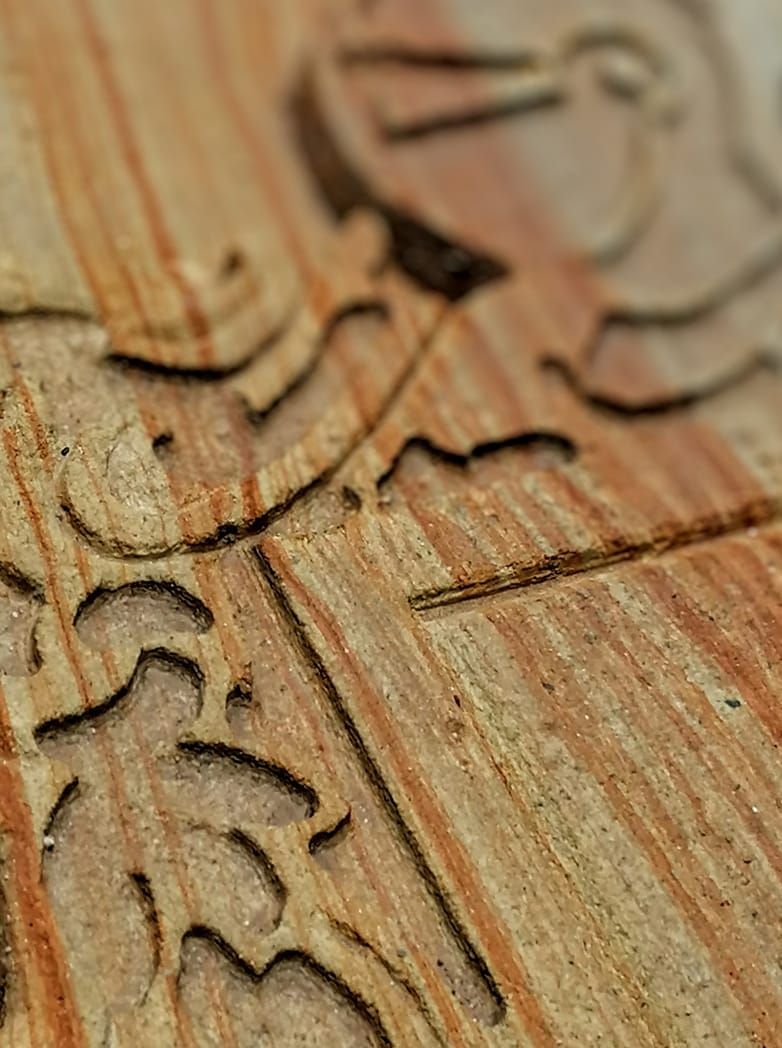 Primer plano y vista en ángulo de una superficie de madera de color marrón claro con intrincados patrones geométricos y en forma de hojas tallados a máquina.