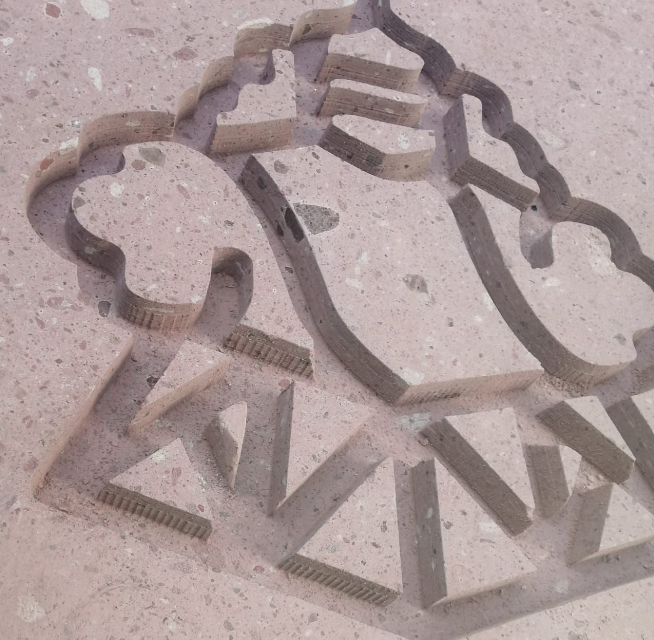 Superficie de piedra rosa con el logotipo de una cabeza de león estilizada tallada, con recortes geométricos y textura.