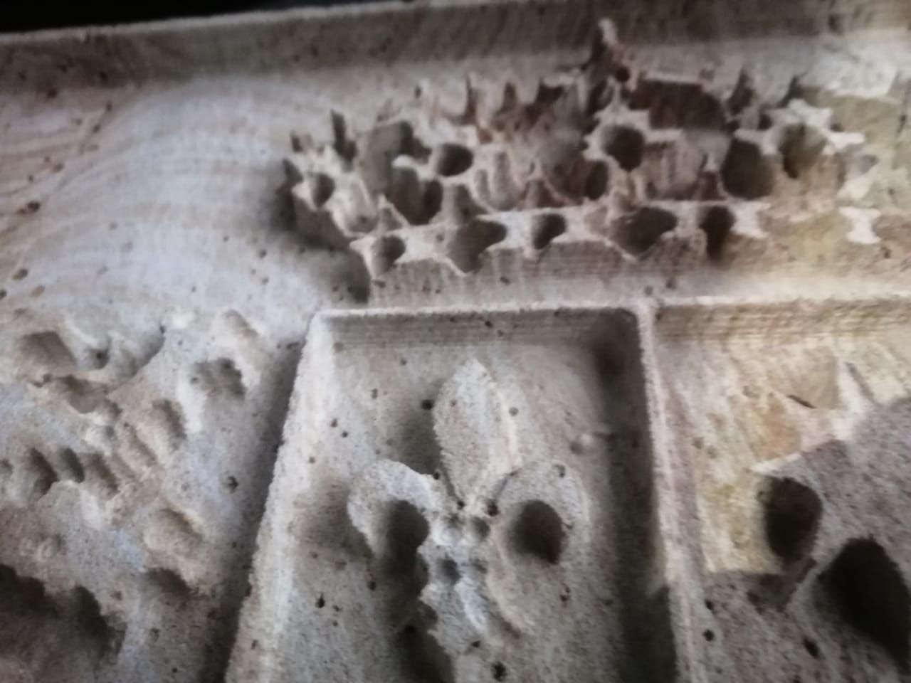 Primer plano de un panel de piedra tallada con un relieve de una corona sobre un símbolo de flor de lis dispuesto en forma de cuadrícula.