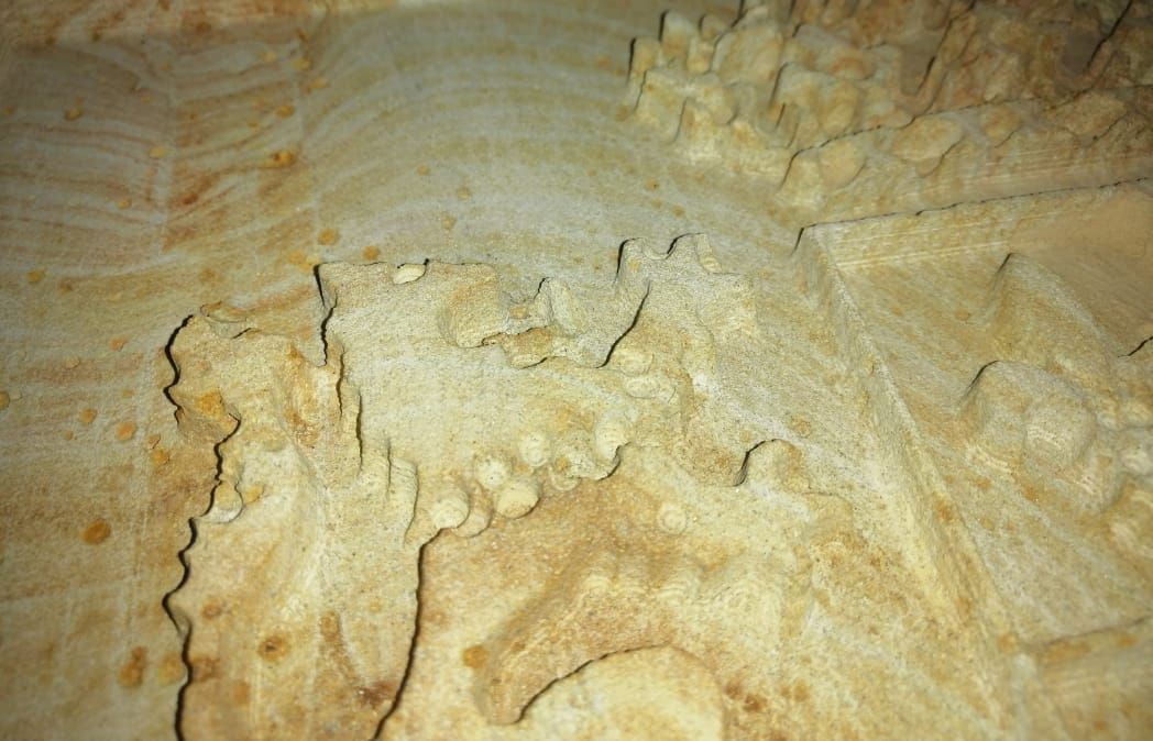 Primer plano de una superficie de piedra tallada de color marrón claro con relieves y bordes texturizados e irregulares.