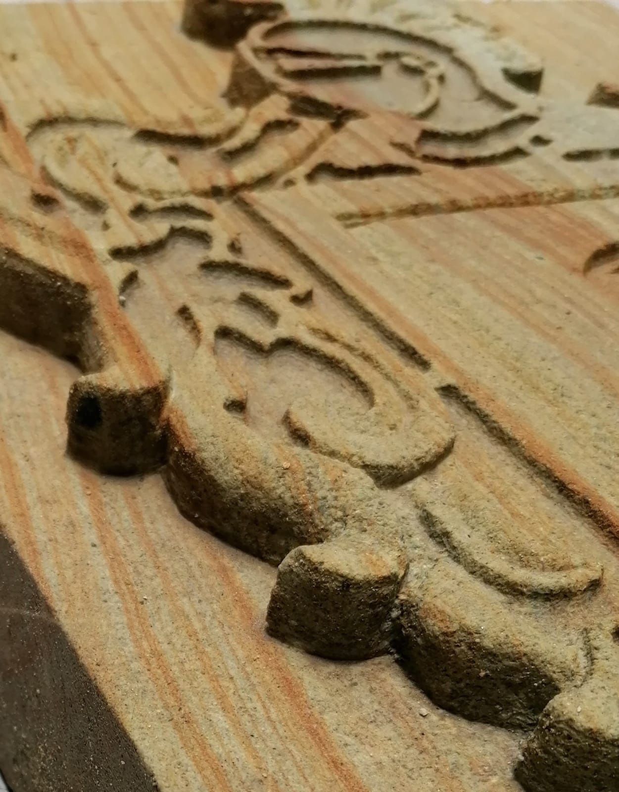 Vista de cerca de un intrincado relieve tallado en madera clara, que muestra diseños de volutas texturizadas y en relieve.