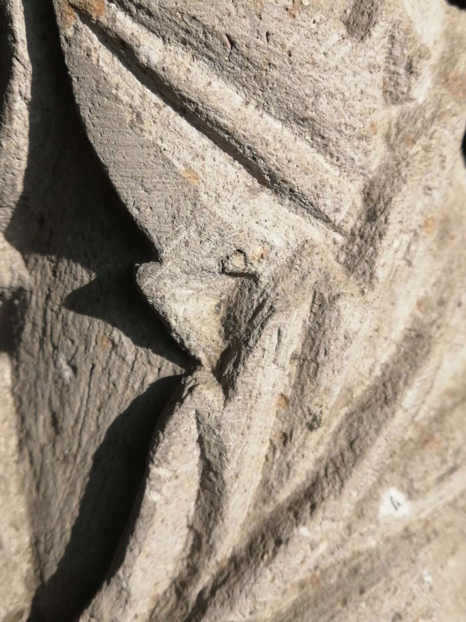 Primer plano de una piedra texturizada de color claro con profundas ranuras diagonales talladas que proyectan sombras nítidas.