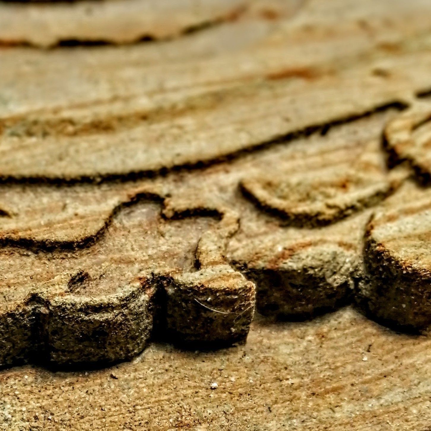 Primer plano de madera tosca y tallada de color marrón claro con intrincados patrones ondulados y profundas líneas texturizadas en relieve.