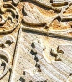 Primer plano de un relieve tallado en piedra beige con intrincados patrones decorativos curvos y superficies texturizadas.