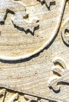 Primer plano de un relieve tallado en piedra beige con intrincados patrones decorativos curvos y superficies texturizadas.