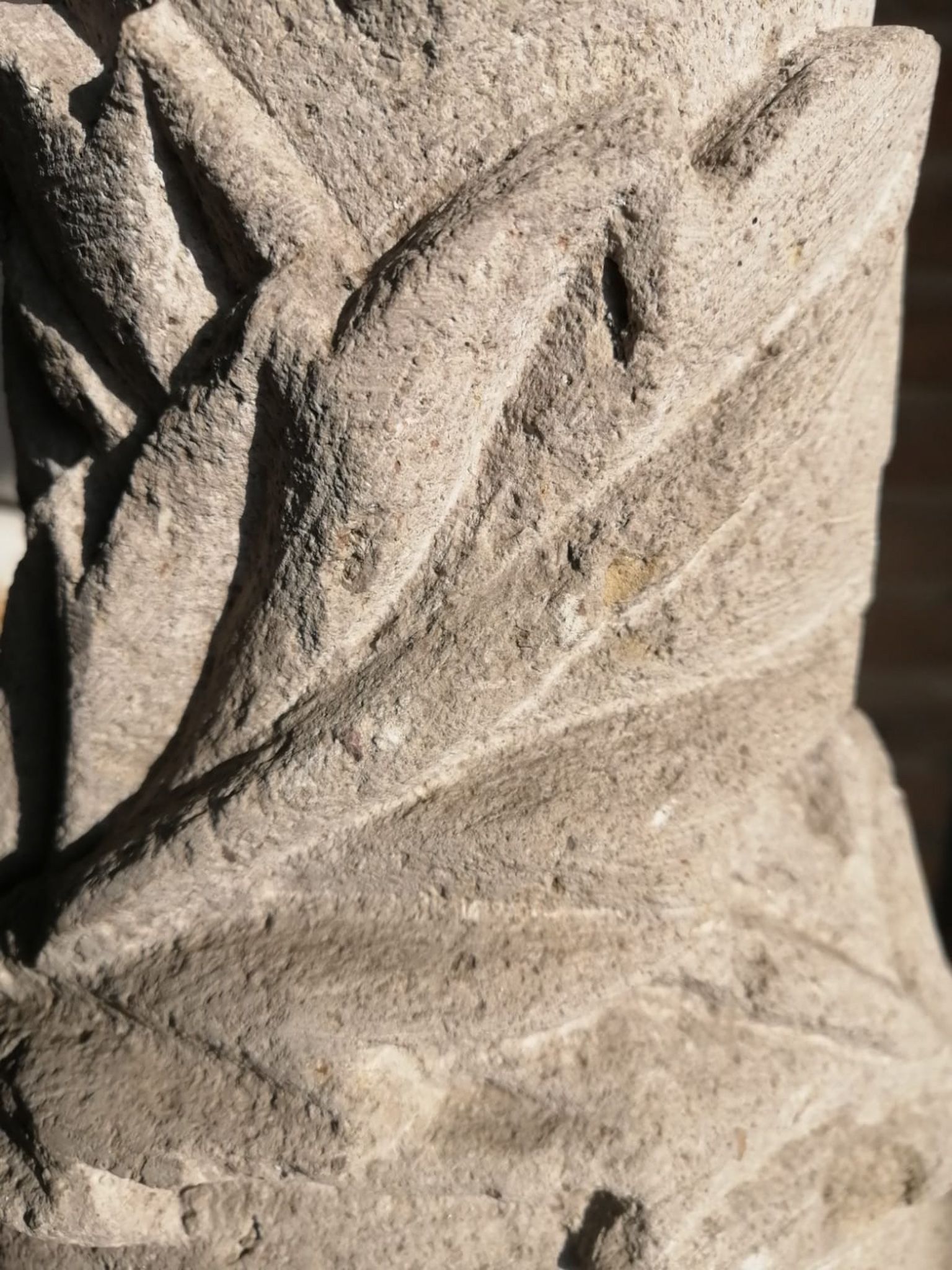 Primer plano de una piedra de color claro tallada con un patrón repetitivo de hojas o plumas en diagonal, en un diseño en relieve.