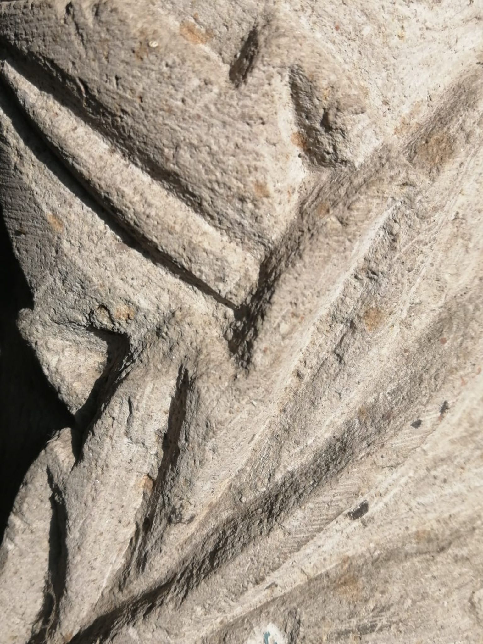 Primer plano de una piedra beige con tallas profundas, angulares y en forma de V, que proyectan sombras dramáticas.