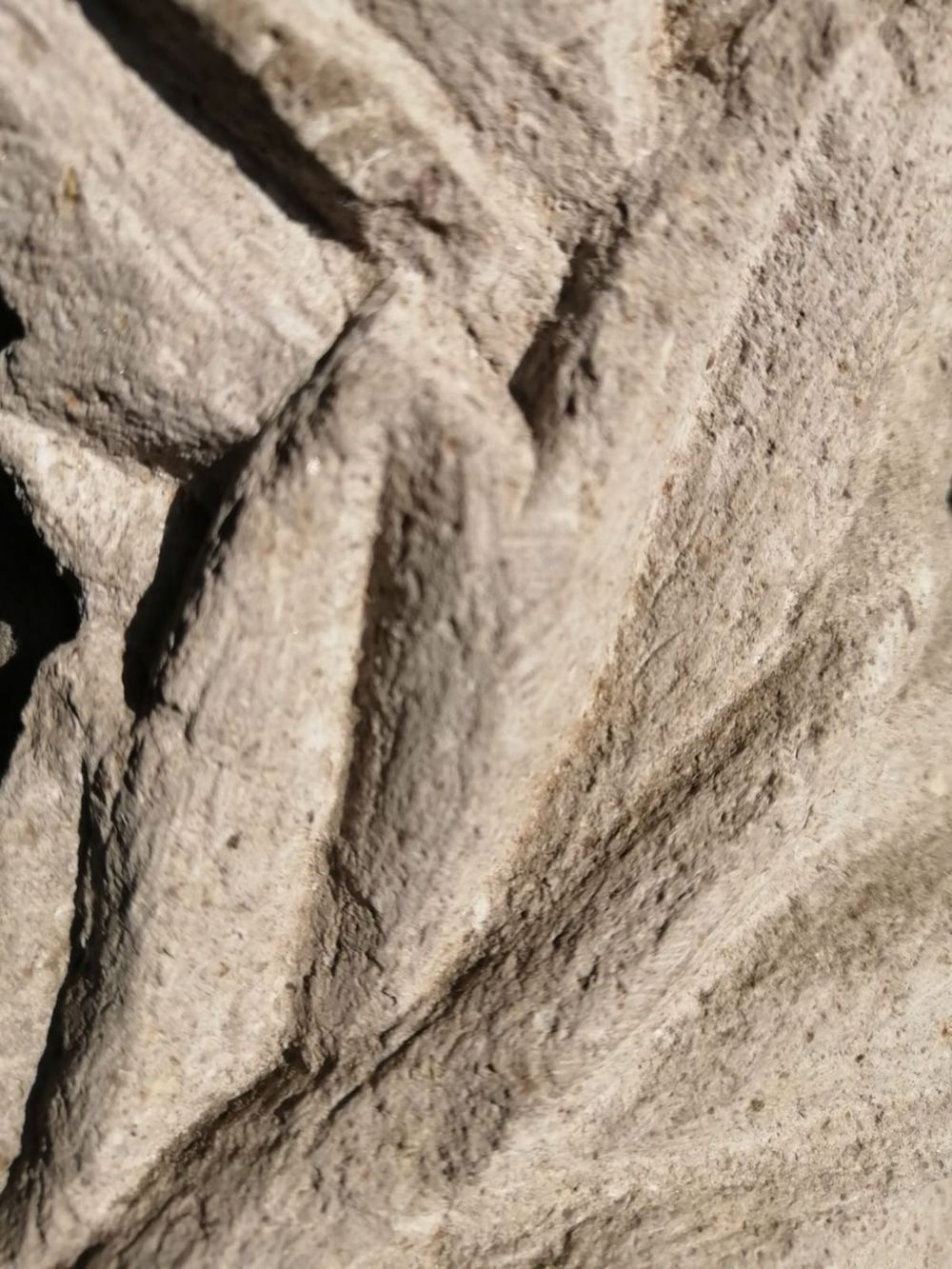 Vista en primer plano, desde arriba, de una superficie de piedra rugosa de color claro con surcos diagonales tallados en forma de espiga.