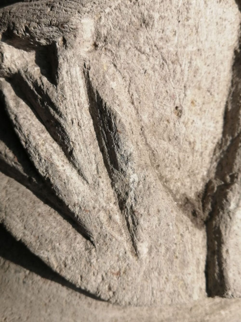 Vista de cerca de una piedra gris tallada y texturizada, con surcos y líneas angulares y diagonales.