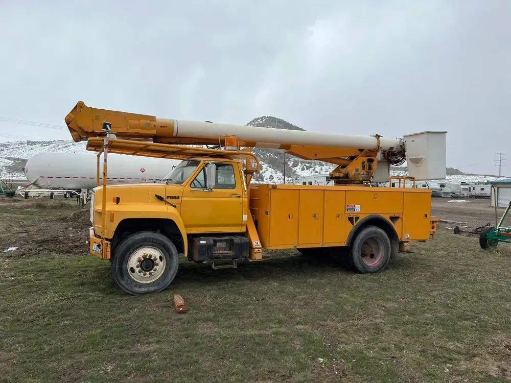 Yellow utility truck with a raised boom in a grassy field.