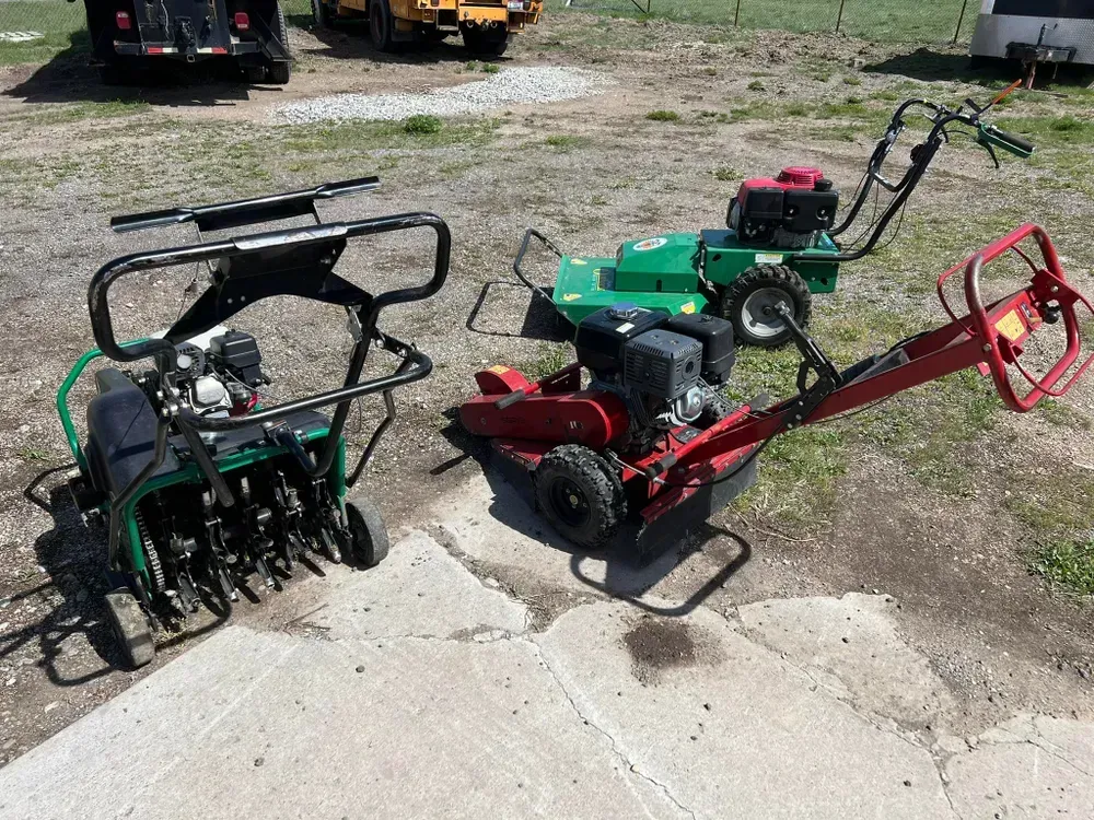 Three landscaping machines: lawn aerator, sod cutter, and tiller on a concrete surface.