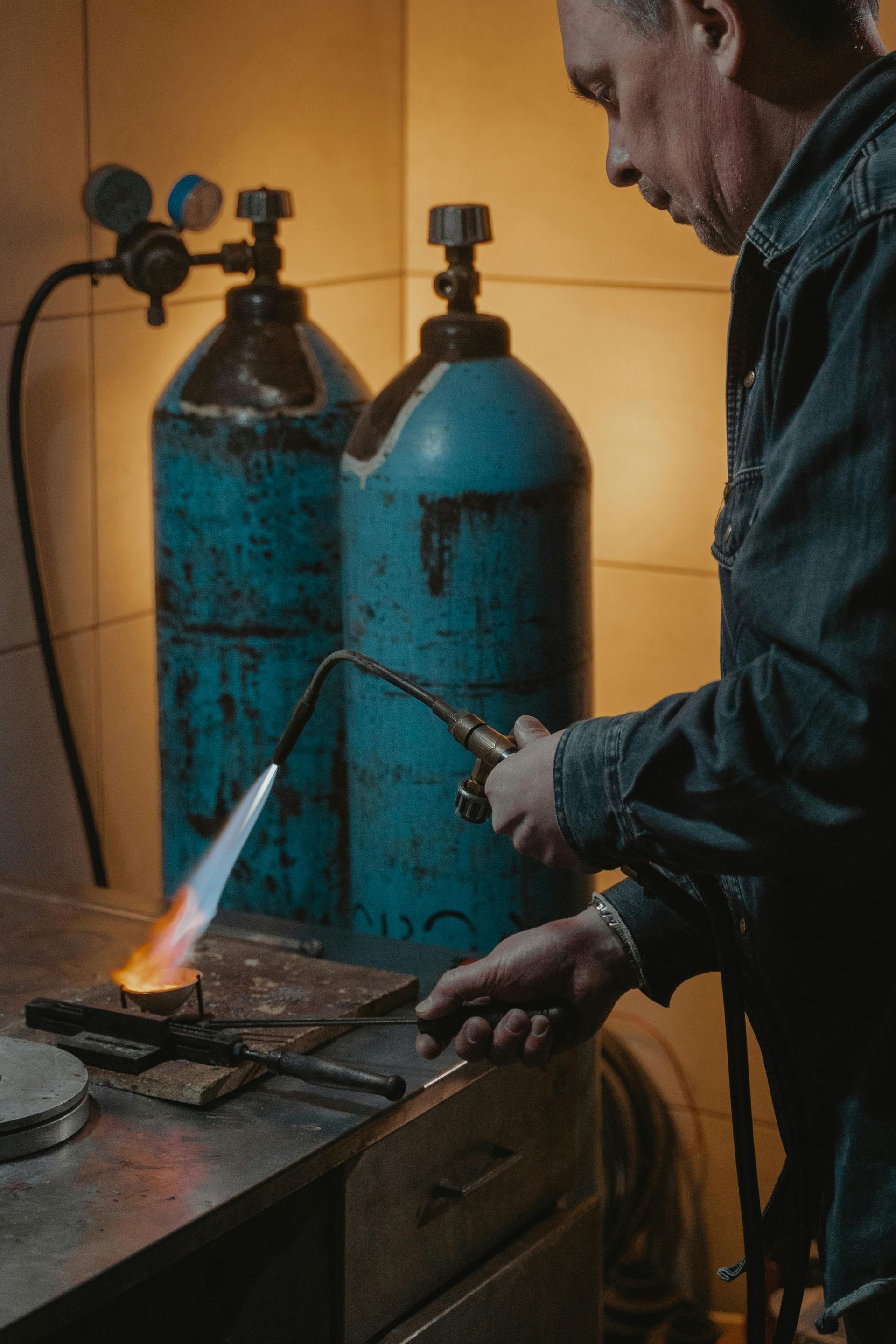 Man welding metal with a torch in a workshop, blue tanks in background.