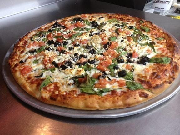 A pizza with tomatoes, olives, spinach, and cheese on a pan.