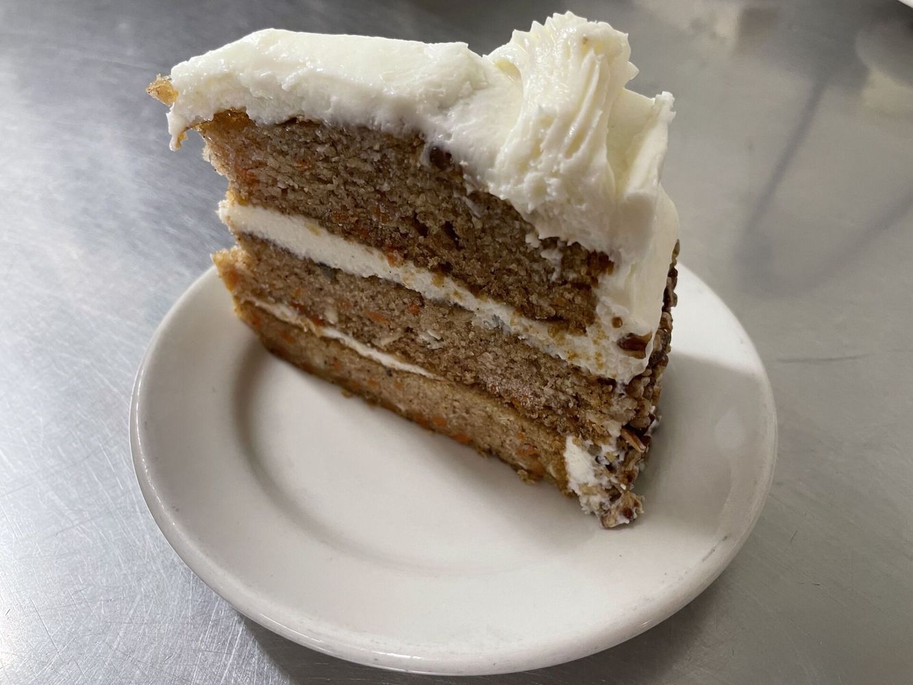 A slice of carrot cake on a white plate on a table.