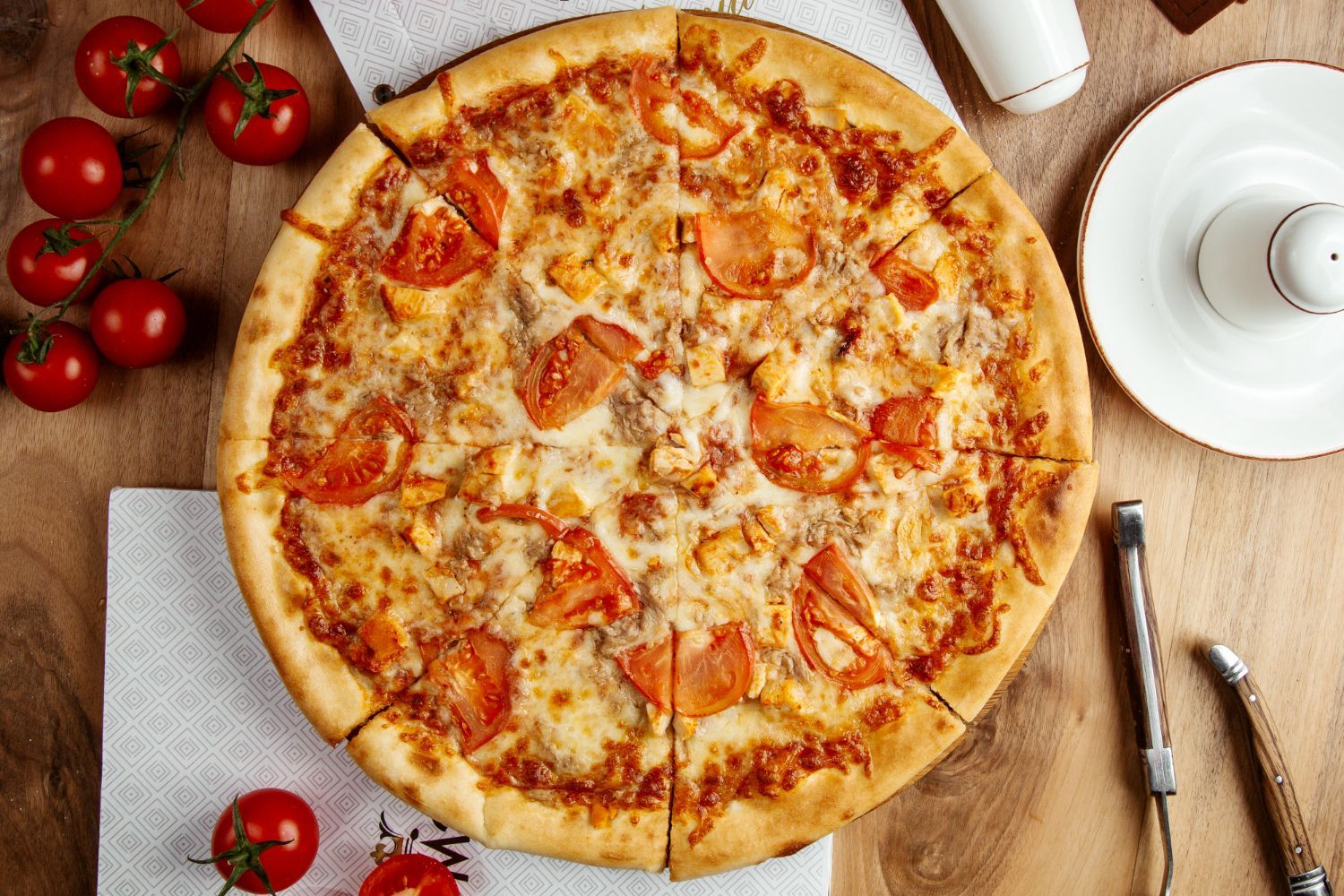 A pizza with tomatoes and cheese is sitting on a wooden table.