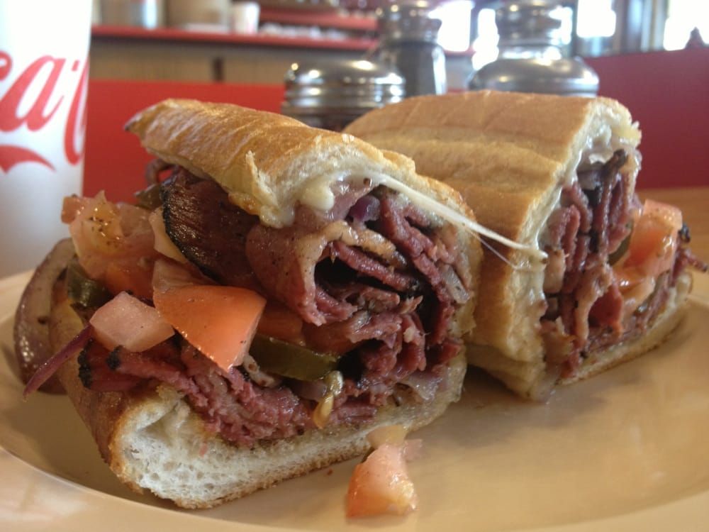A sandwich on a white plate with a coca cola cup in the background.
