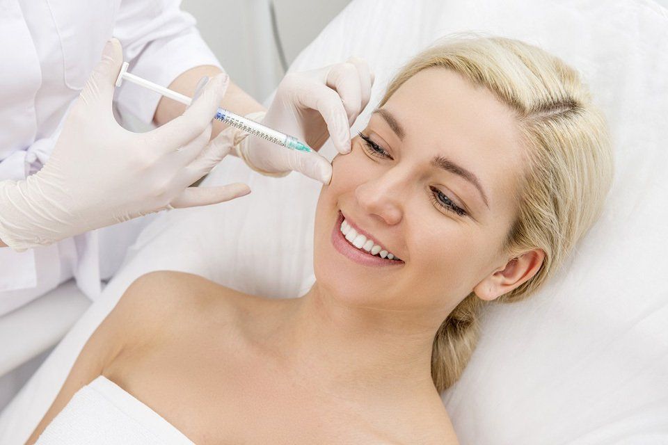 Uma mulher está sorrindo enquanto recebe uma injeção de botox no rosto.