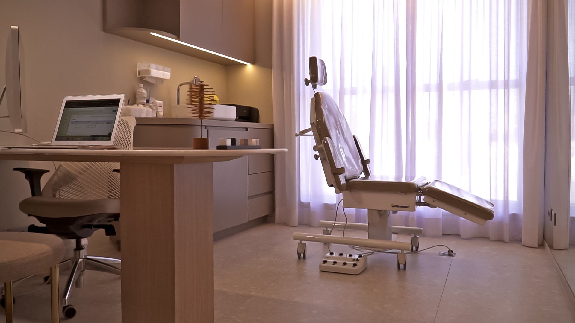 Um consultório médico com uma cadeira odontológica e uma mesa com um laptop.