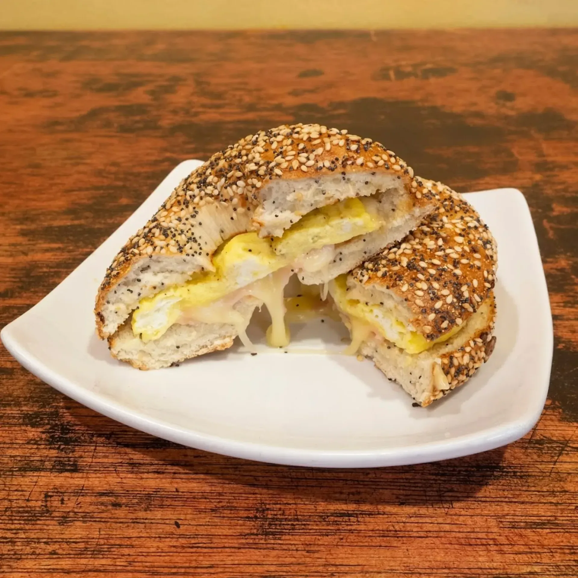 Bagel sandwich cut in half on a white plate, showing melted cheese and egg inside.