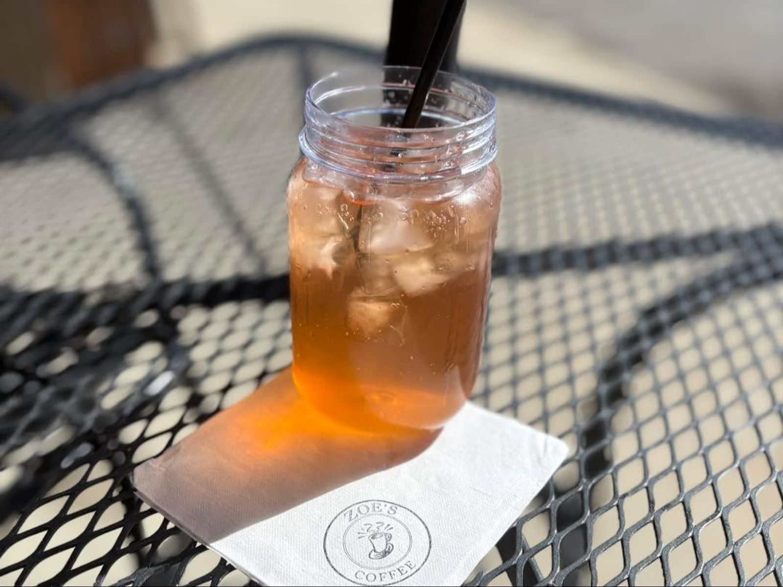 Iced tea in a mason jar with a straw on a table with sunlight and a napkin.