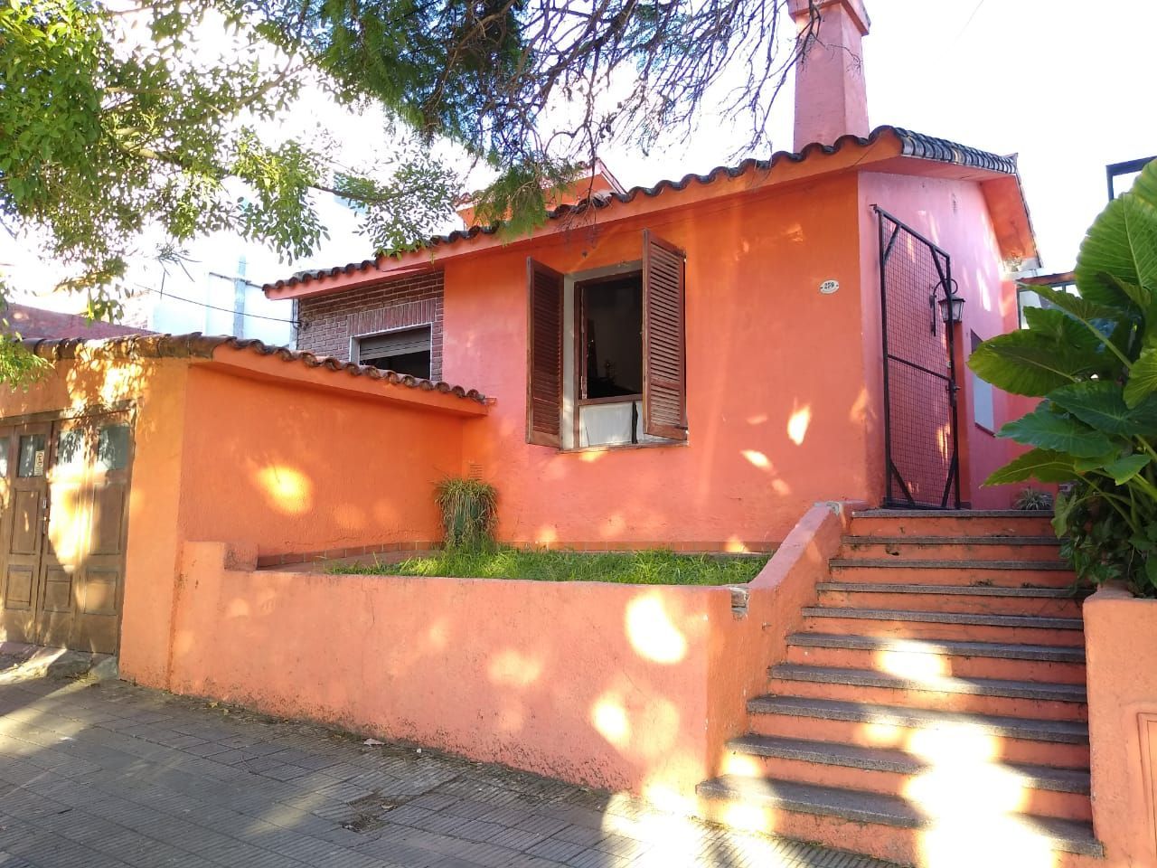 Casa de estuco naranja con ventana abierta, pequeño césped y escalones que conducen hacia arriba.