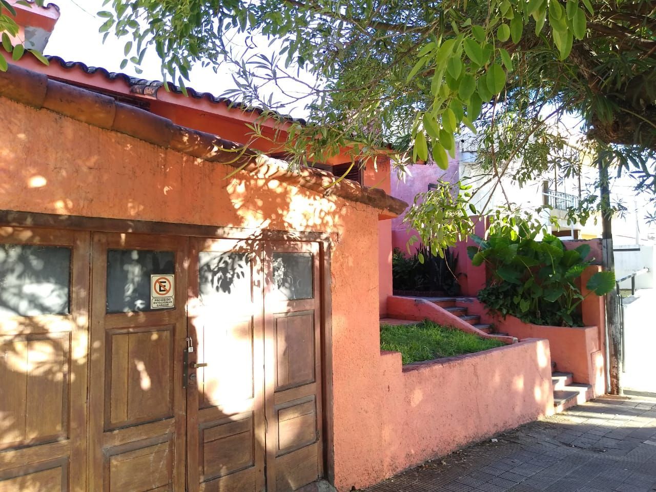 Casa de estuco naranja con ventana abierta, pequeño césped y escalones que conducen hacia arriba.