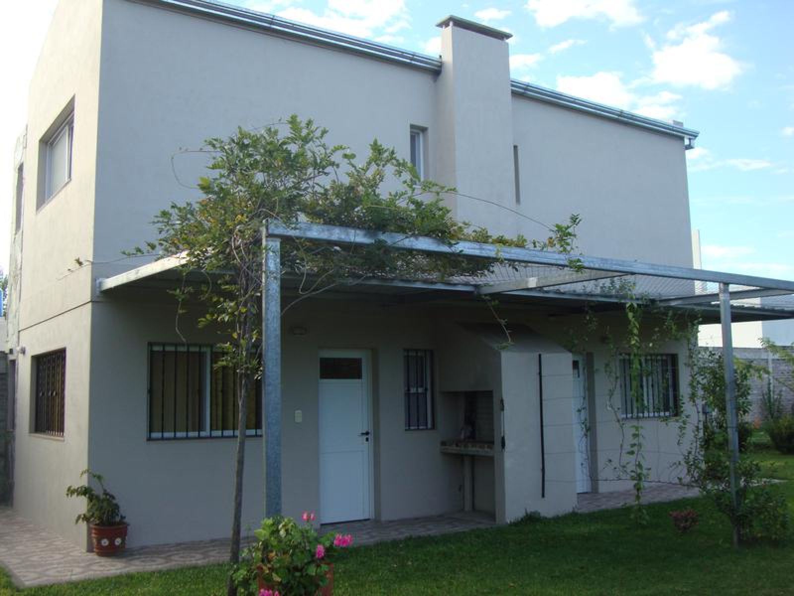 Verja de hierro forjado negro con puerta de columnas blancas, frente a una casa de color claro.