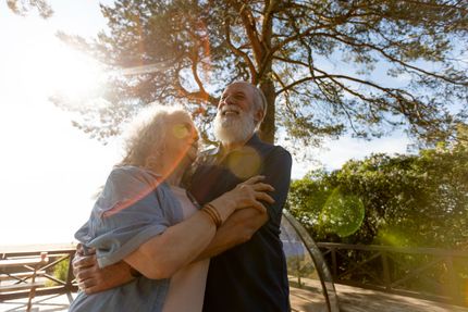A man and a woman are hugging each other in front of a tree.