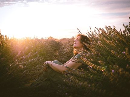 A woman is sitting in a field of flowers with her eyes closed.