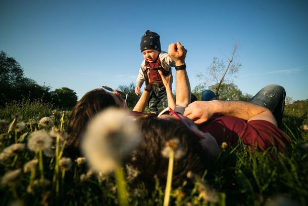 A man is laying in the grass holding a baby in his arms.
