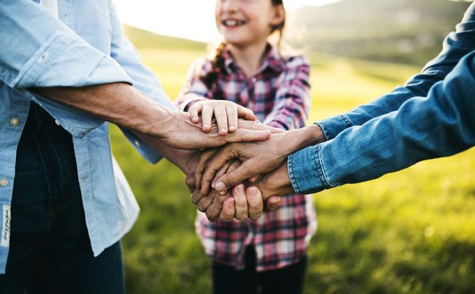 A family is putting their hands together in a field.