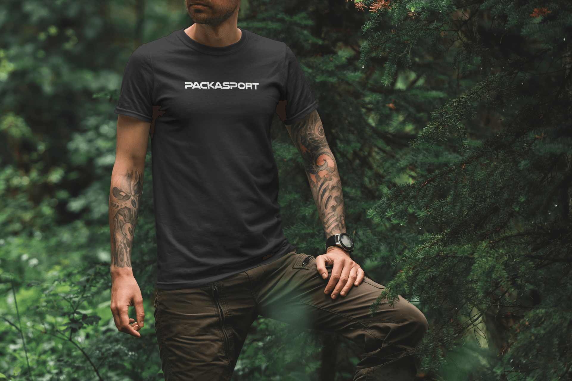 A man wearing a black t-shirt is standing in the woods.